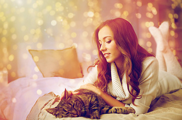 Image showing happy young woman with cat lying in bed at home