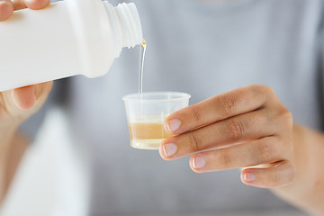 Image showing woman pouring syrup from bottle to medicine cup