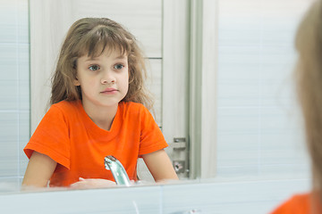 Image showing Seven-year-old girl looks at herself in the mirror, in the bathroom