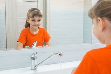 Image showing Seven-year-old girl washing her face looks at herself in the mirror