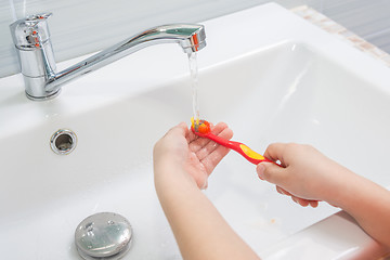 Image showing The child rinses the toothbrush under running water