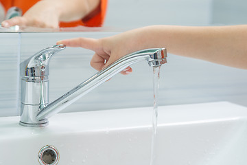 Image showing The child\'s hand closes the water from the mixer by pressing the finger on the handle