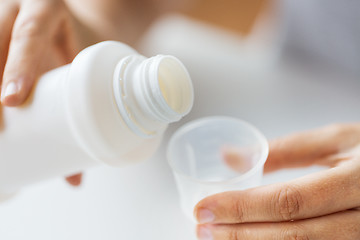 Image showing woman pouring syrup from bottle to medicine cup