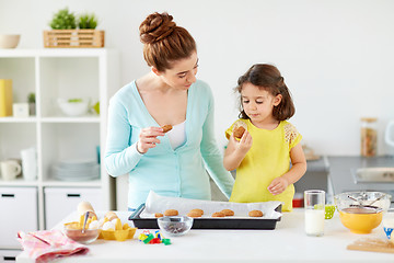 Image showing happy mother and daughter eating cookies at home