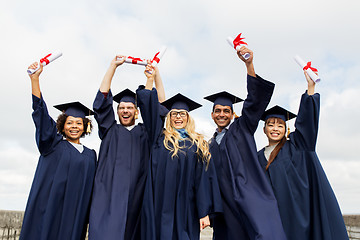 Image showing happy students in mortar boards with diplomas