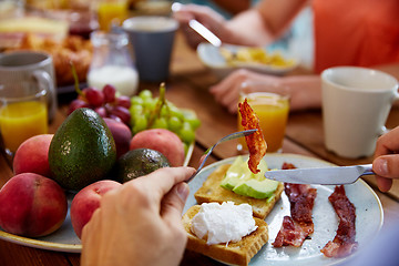 Image showing hands with bacon on fork at table full of food