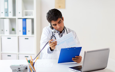 Image showing doctor with clipboard calling on phone at clinic