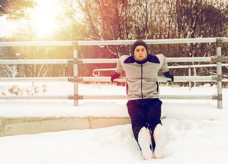 Image showing sports man doing triceps dips at fence in winter