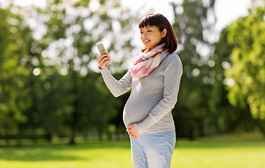 Image showing happy pregnant asian woman taking selfie at park