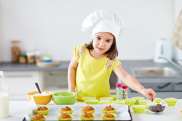 Image showing little girl in chefs toque baking muffins at home