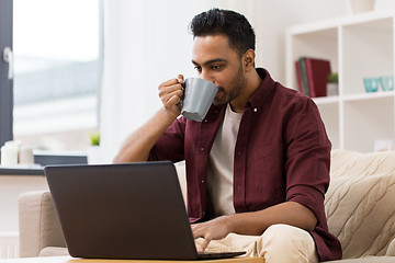 Image showing smiling man with laptop drinking coffee at home