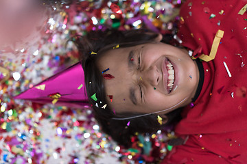 Image showing kid blowing confetti while lying on the floor