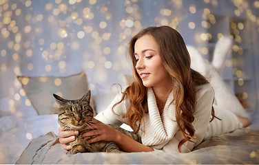 Image showing happy young woman with cat lying in bed at home