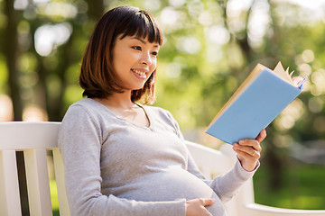 Image showing happy pregnant asian woman reading book at park