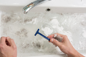 Image showing The man is shaving, the view of the hands with a razor and the wash basin with dirty water