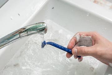 Image showing The man\'s hand washes the shaver under the stream of water, close-up on top