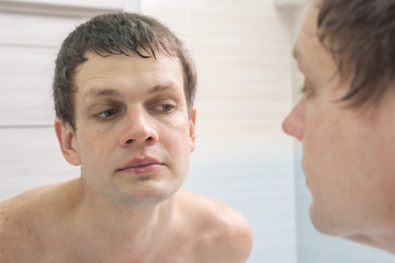 Image showing A clean-shaven young man looks in the mirror