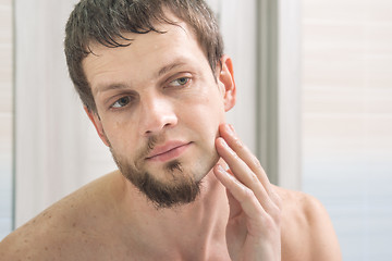 Image showing The guy shaved one half of his face and looks in the mirror evaluating the result