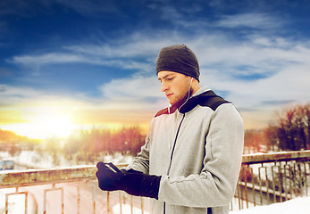 Image showing man in earphones with smartphone on winter bridge