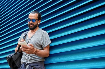 Image showing man with earphones and smartphone over wall