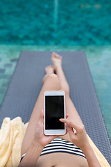 Image showing Woman relax on sunbath in swimming pool with using mobile phone