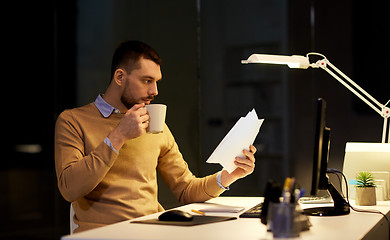 Image showing man with papers and coffee working at night office