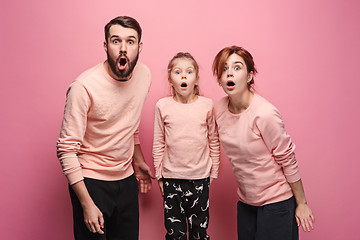 Image showing Surprised young family looking at camera on pink