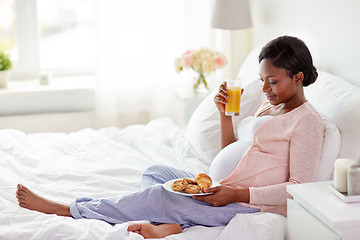 Image showing pregnant woman with orange juice and pastry in bed