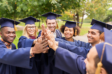 Image showing happy students in mortar boards making high five