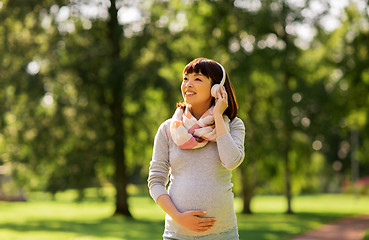 Image showing happy pregnant asian woman in headphones at park