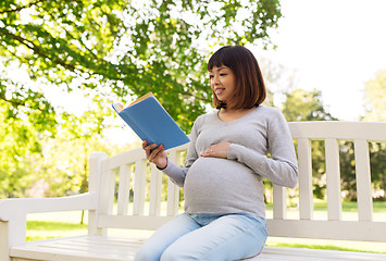 Image showing happy pregnant asian woman reading book at park