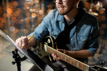 Image showing man with guitar writing to music book at studio