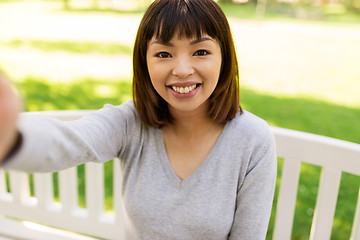Image showing happy smiling asian woman taking selfie at park