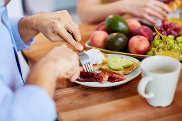 Image showing man with fork eating bacon at table full of food