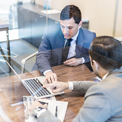 Image showing Two young businessmen using laptop computer at business meeting.