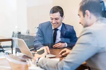 Image showing Two young businessmen using laptop computer at business meeting.