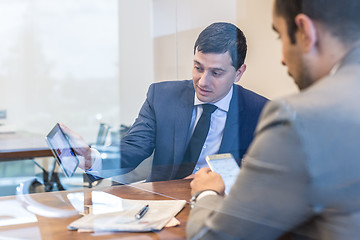 Image showing Two young businessmen using electronic devices at business meeting.