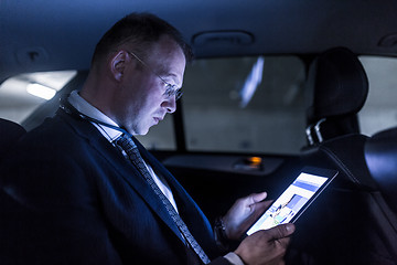 Image showing Businessman with a digital tablet sitting in the back seat of a car