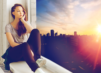 Image showing sad pretty teenage girl sitting on windowsill