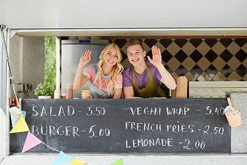 Image showing happy couple of sellers waving hands at food truck