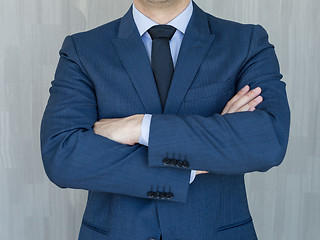 Image showing Torso of a businessman standing with folded arms in a classic navy blue suit.