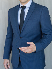 Image showing Torso of a businessman standing, making italian hand gesture, wearing navy blue suit.