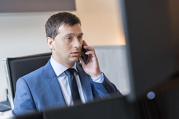 Image showing Businessman talking on mobile phone while watching charts and data analyses on multiple computer screens.