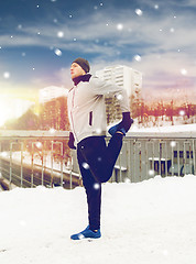 Image showing man exercising and stretching leg on winter bridge