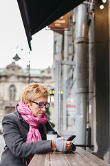 Image showing Woman browsing smartphone in outside cafe