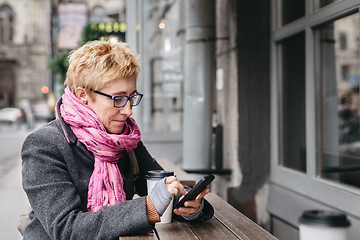 Image showing Woman browsing smartphone in outside cafe