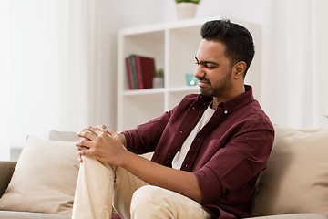 Image showing unhappy man suffering from pain in leg at home