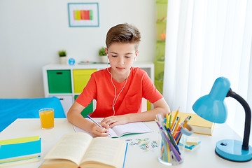 Image showing student boy in earphones writing to notebook