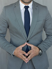 Image showing Torso of anonymous businessman standing with hands in lowered steeple wearing beautiful fashionable classic grey suit, white shirt and blue tie.