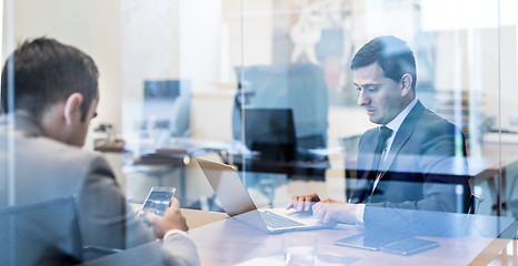 Image showing Two young businessmen using laptop computer at business meeting.